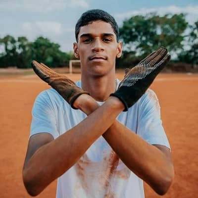 Iran Ferreira posing on a football field wearing a white shirt and gloves crossed in front of his chest.