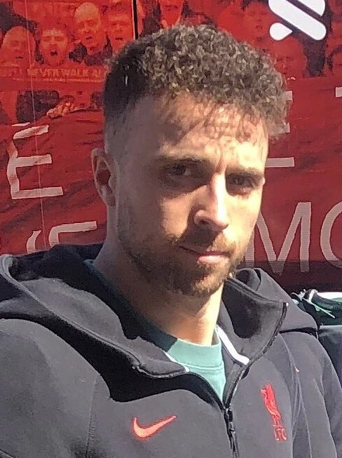 Diogo Jota in a Liverpool jacket, photographed outdoors in front of a red backdrop.